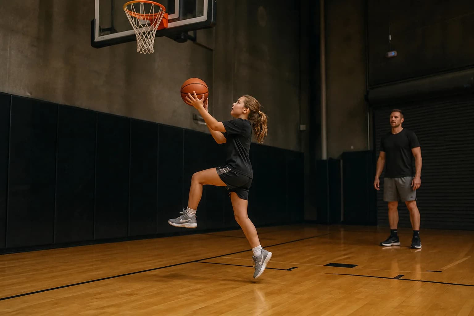 A young player practising a layup while a coach observes